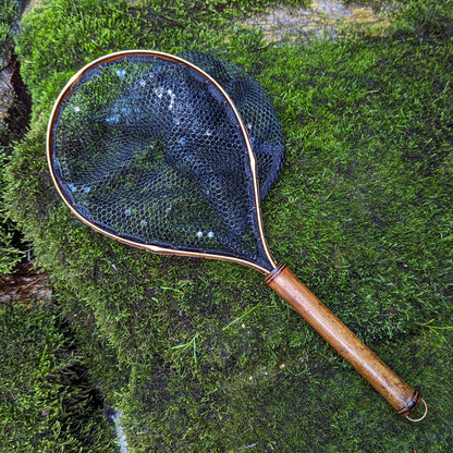 A bamboo fly fishing net lying on a rock in the water on the river in Western North Carolina. The rubber net basket is smooth and shiny and protects the fish for catch and release. The handle is flame cured for strength and durability and there is copper stitching and a copper keeper ring to attach your net keeper to.