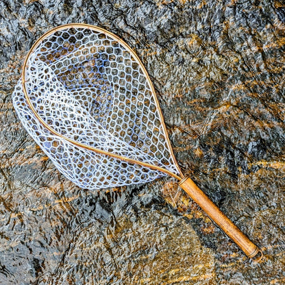 A bamboo fly fishing net lying on a rock in the water on the river in Western North Carolina. The rubber net basket is smooth and shiny and protects the fish for catch and release. The handle is flame cured for strength and durability and there is copper stitching and a copper keeper ring to attach your net keeper to.