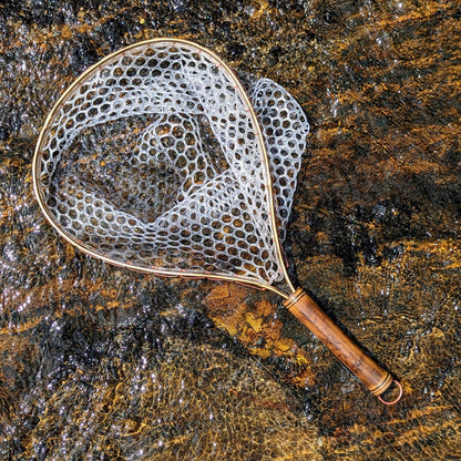 A bamboo fly fishing net lying on a rock in the water on the river in Western North Carolina. The rubber net basket is smooth and shiny and protects the fish for catch and release. The handle is flame cured for strength and durability and there is copper stitching and a copper keeper ring to attach your net keeper to.